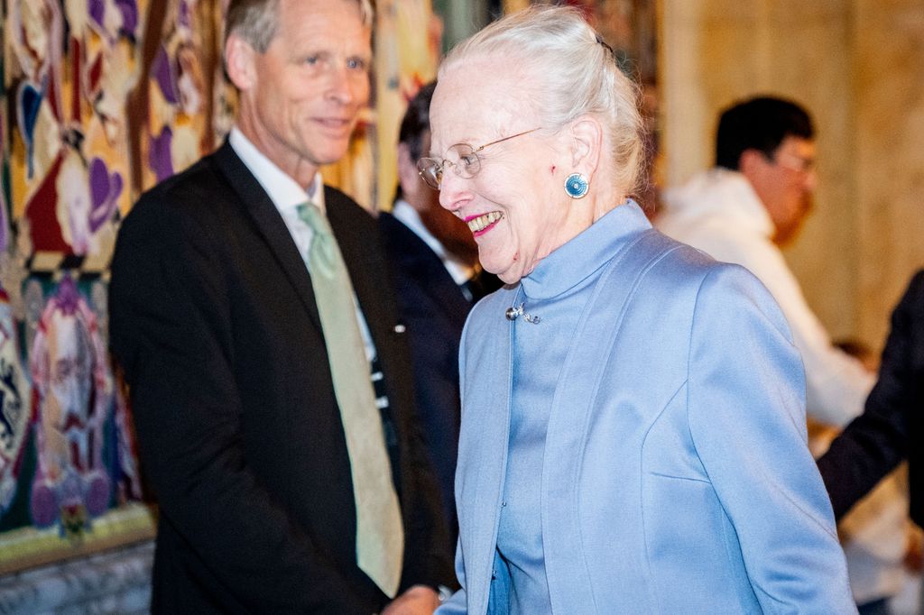 Queen Margrethe in a blue dress walking past a man in a black suit