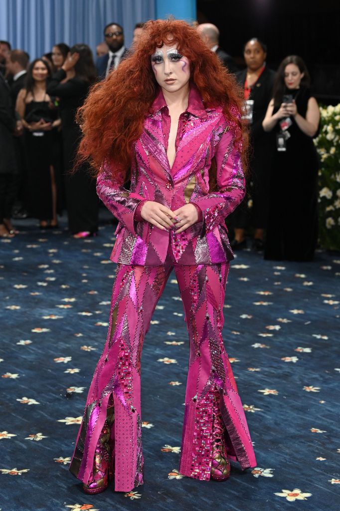 Chappell Roan wears a bright pink sequin striped suit with a dagger collar and flared trousers.