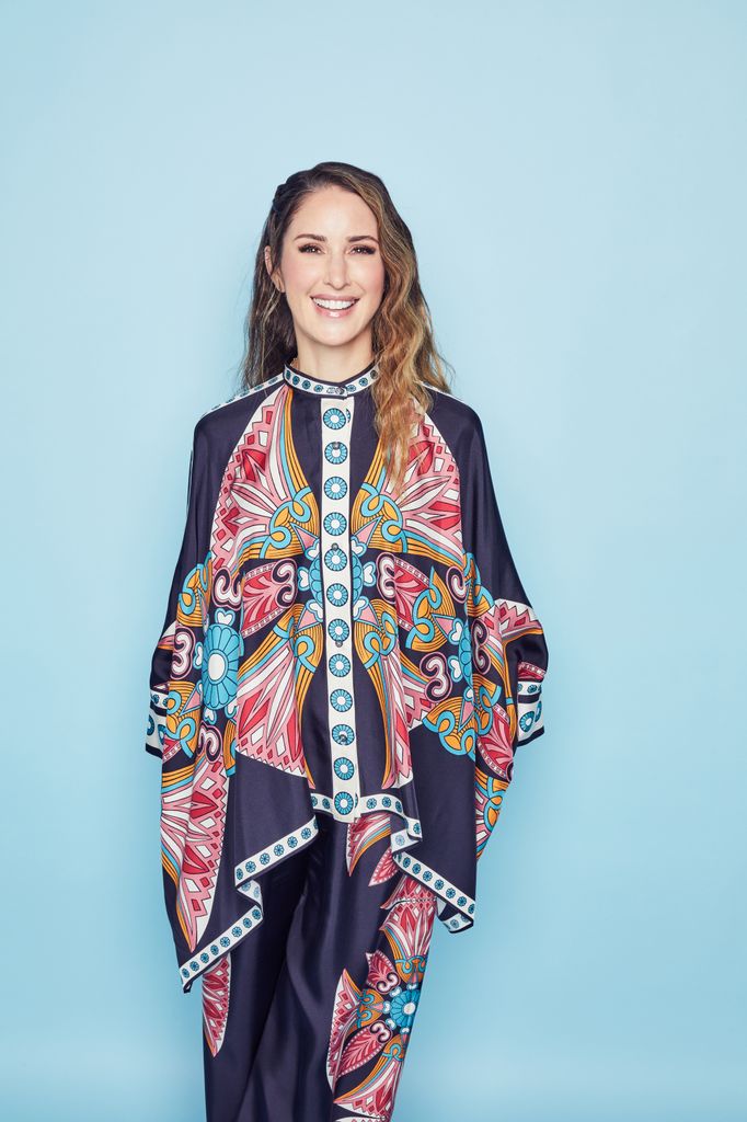 woman in printed waterfall top smiling for the camera against a baby blue wall