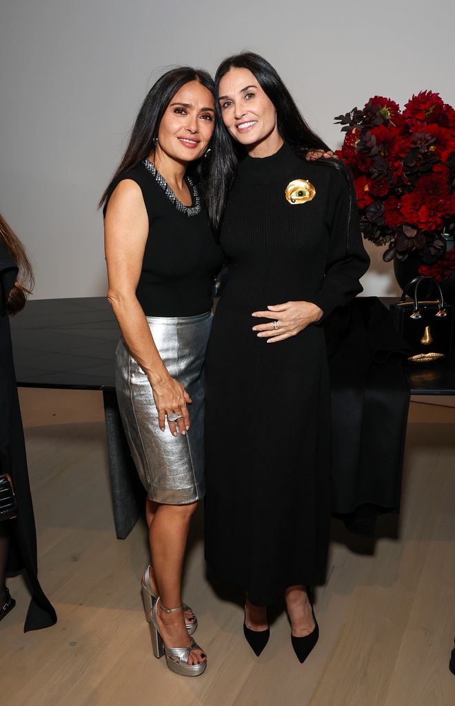 Salma Hayek in black top and silver skirt posing with Demi Moore at  Sami Hayek's show: FREQUENCY at Christie's Beverly Hills  