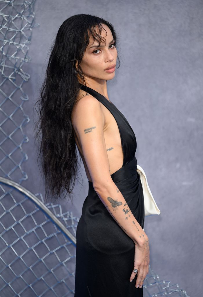 Zoë Kravitz in her amazing Saint Laurent dress on the red carpet. She looks to the side - her tattooes on her arms showcased, and her long tousled black hair with a slight wave