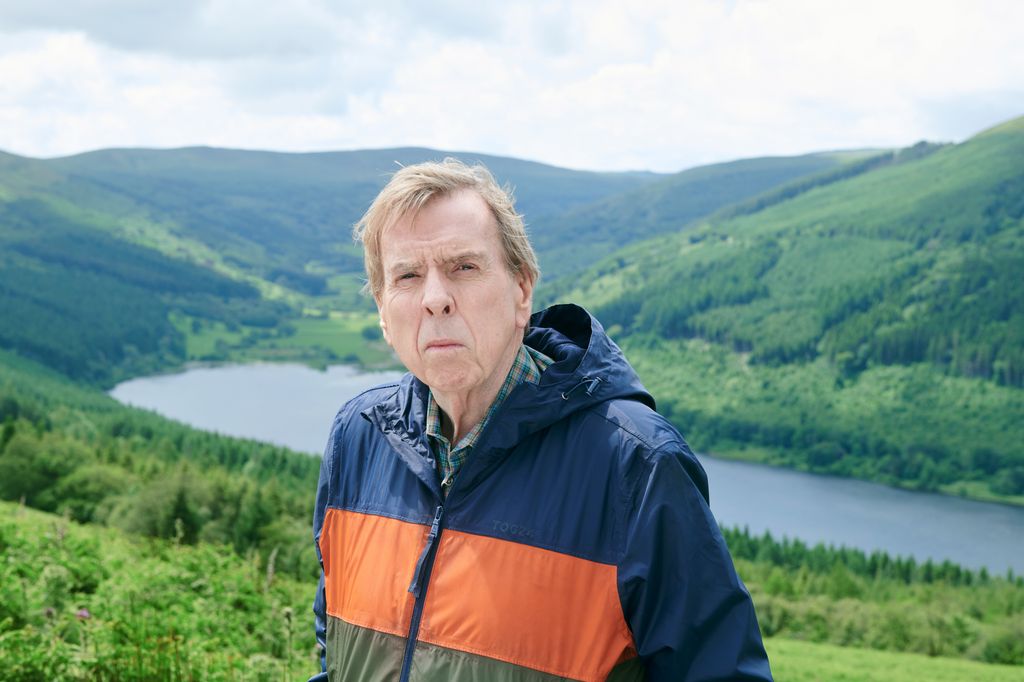 man in rain coat standing in front of lake