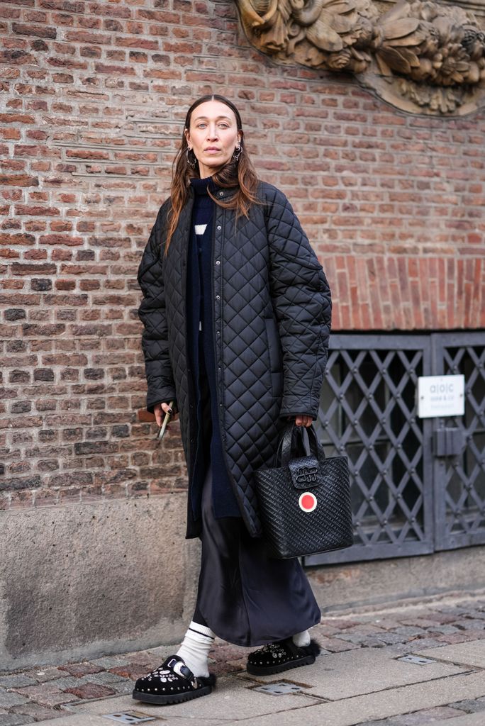 COPENHAGEN, DENMARK - JANUARY 31: Alana Hadid wears earrings, a black padded / quilted long jacket , a dark blue turtleneck pullover , a long cardigan, a bag with embossed monograms, a black skirt , white socks, black sandals, outside The Garment, during the Copenhagen Fashion Week AW24 on January 31, 2024 in Copenhagen, Denmark. (Photo by Edward Berthelot/Getty Images)