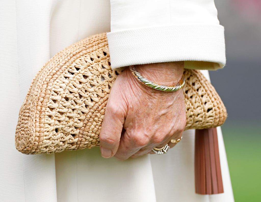 Queen Camilla holding a raffia clutch bag, wearing a gold bracelet