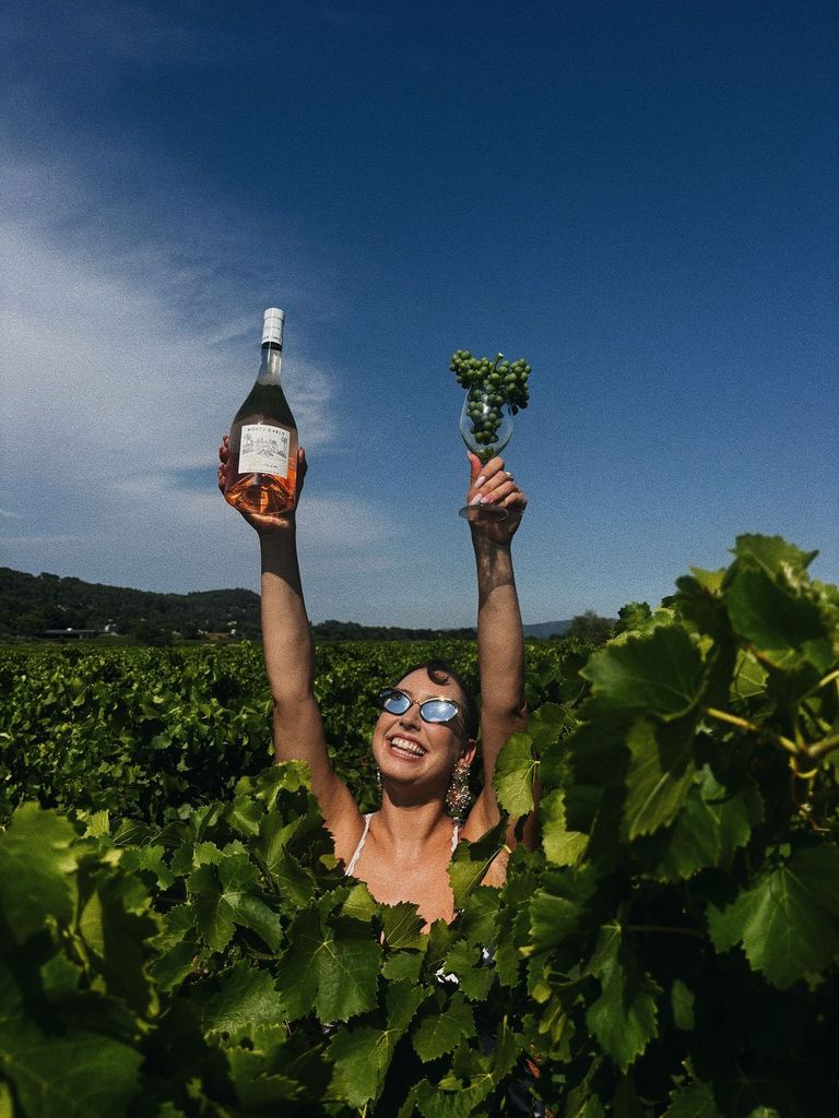 Woman in a vineyard with her arms in the air holding wine