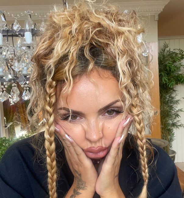 a close up photo of jesy pressing both hands onto her cheeks with her head tilted down to show her blondish wavy hair piled high on top of her head with two long braids falling on either side of her face
