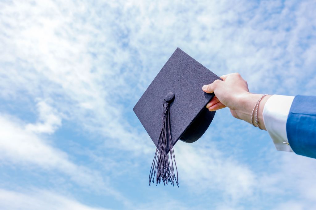 A close-up shot of a student's hand throwing a hat into the sky during a graduation celebration