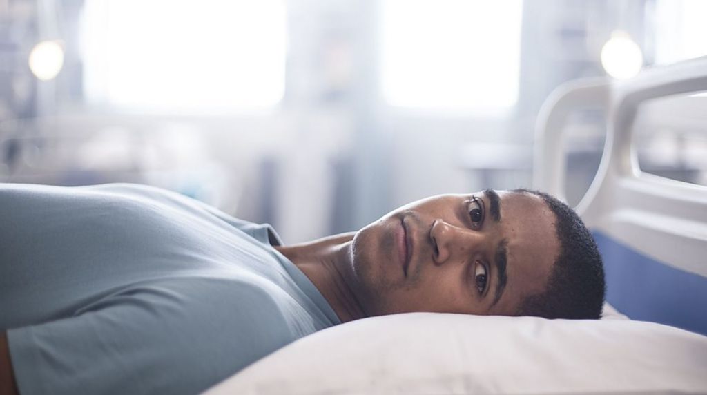 Alfred Enoch lying in a hospital bed in Trust Me