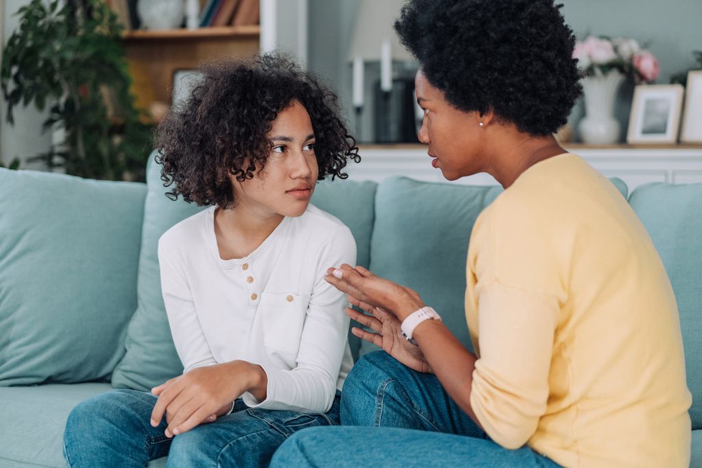 mother talking with her upset teenager on the sofa in the living room.