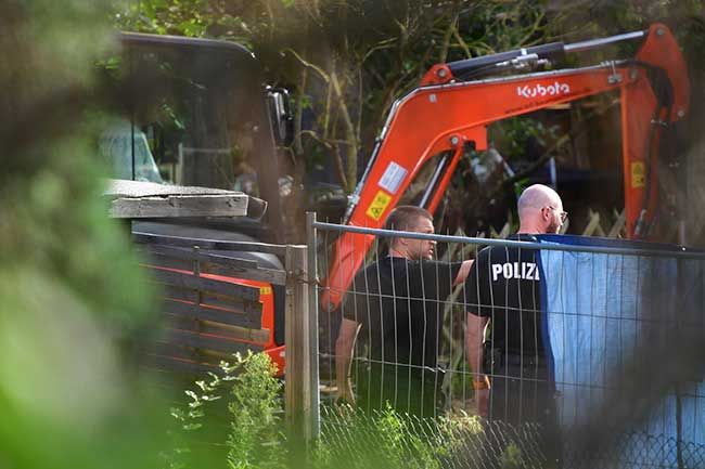A digger and some police officers searching a gated off area of land