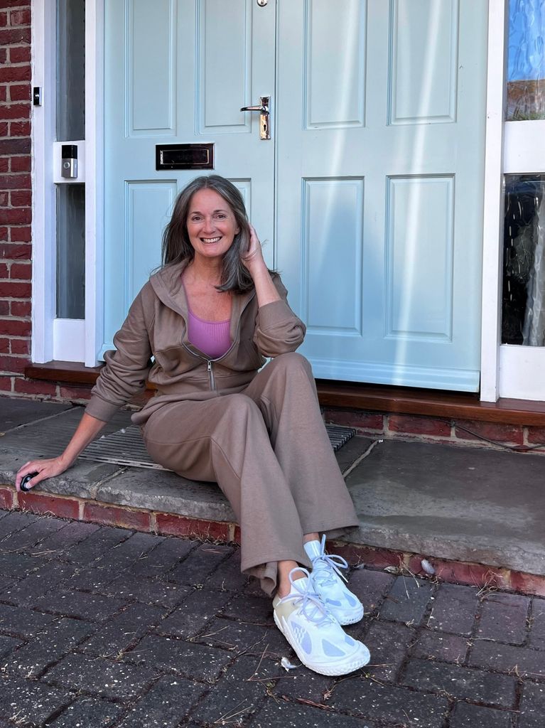 Woman sitting in a taupe tracksuit with a pink top underneath