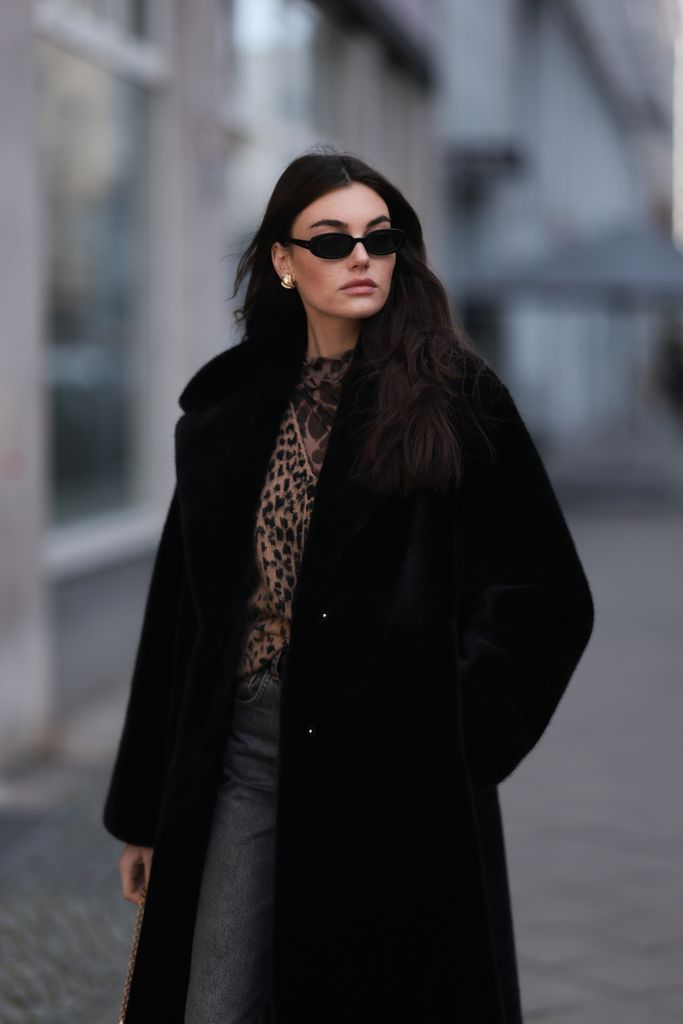 Celine Bethmann seen wearing Dior gold earrings, Le Specs black oval sunglasses, Jaded London brown leopard pattern wool knit cardigan jacket, Levi's Vintage grey denim straight leg jeans / long pants, HermÃ¨s Kelly black leather belt, black vintage long fake fur coat, Gucci black leather / gold bag, on February 07, 2024 in Berlin, Germany. 