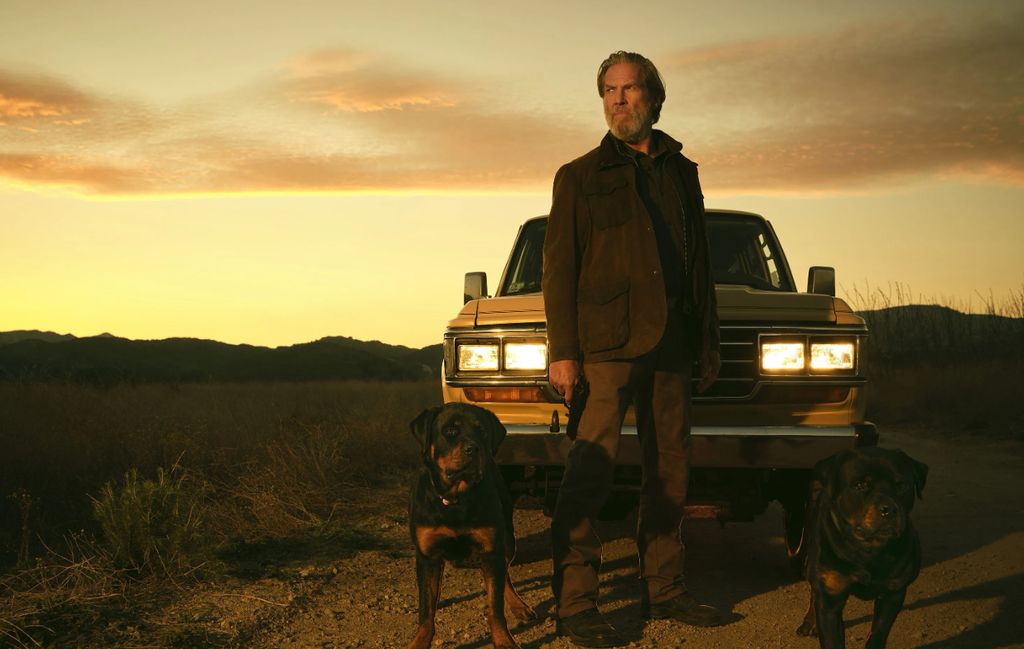 Jeff Bridges standing in front of a pick-up truck with two Rottweilers in The Old Man