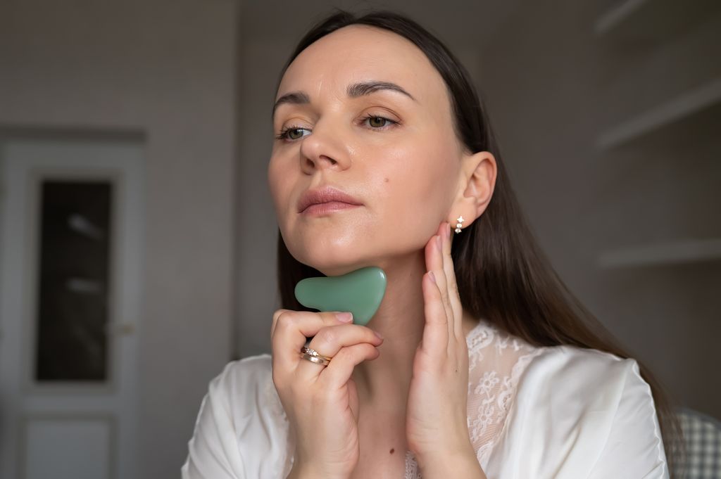 woman using gua sha on neck with skincare