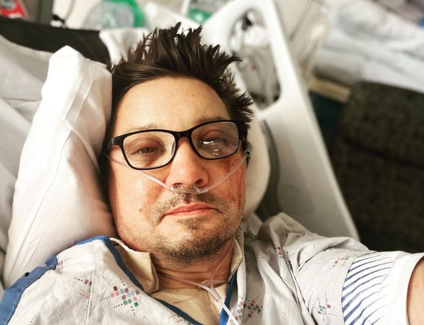 Jeremy Renner lying in a hospital bed with slightly bloodied face