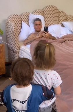 Robbie Williams liegt im Bett, während seine Kinder ihm etwas vorsingen