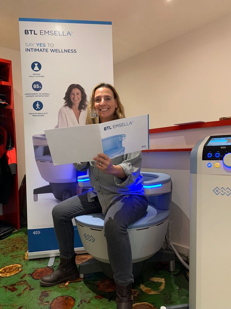 Woman smiling while sitting on an emsella chair reading a brochure