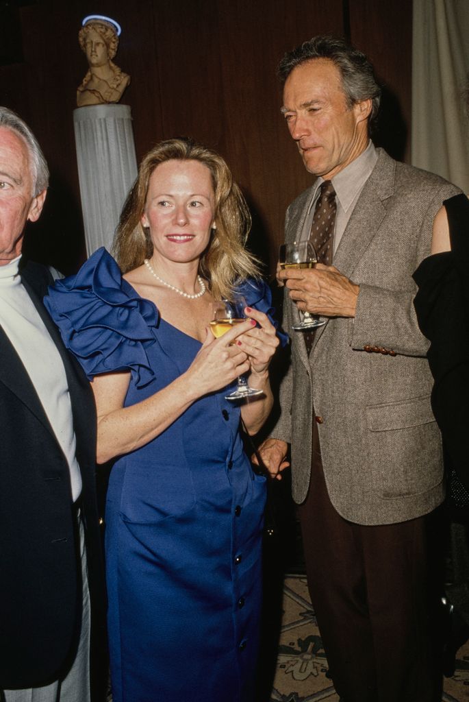 Clint Eastwood, wearing a grey tweed blazer over a beige shirt with a brown polka dot tie, and Jacelyn Reeves, who wears a blue ruffle sleeve dress, attend a reception at the AT&T Pebble Beach Pro-Am golf tournament, in Pebble Beach, California, circa 1987