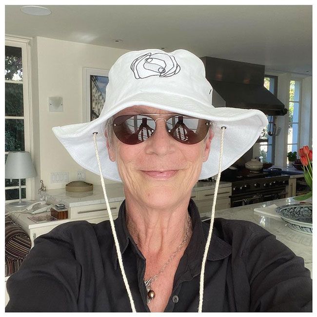 jamie lee curtis takes a selfie in her kitchen wearing a hat