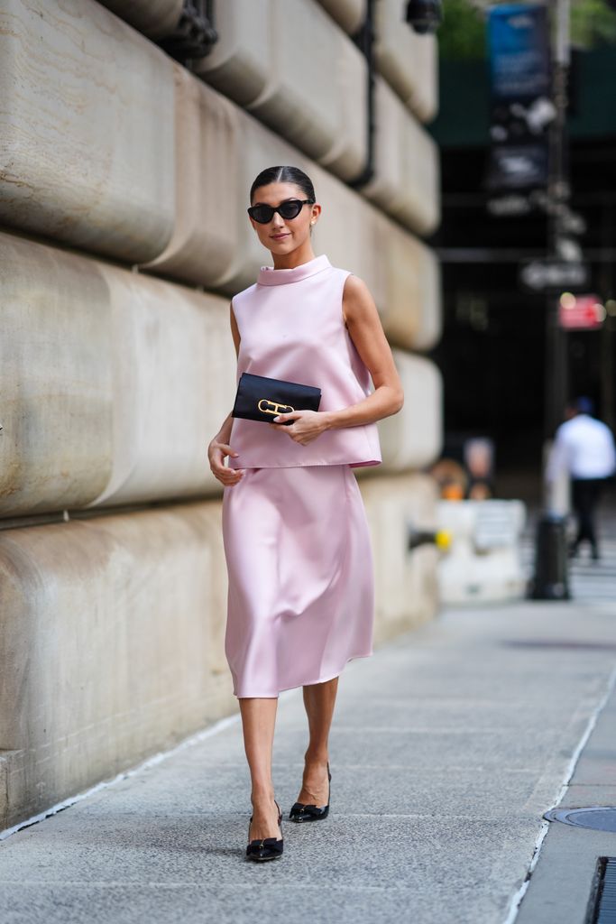 Kate Bartlett wears black PTEMBER 09: sunglasses, white earrings, light pink sleeveless Carolina Herrera shirt, light pink Carolina Herrera midi skirt, black Carolina Herrera clutch handbag, shiny black slingback kitten heels, outside Carolina Herrera, during the New York Fashion week Spring/Summer 2025 on September 9, 2024 in New York, New York.