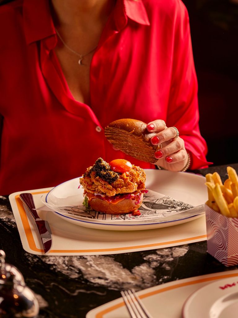 chicken burger on table, with women lifting the top bun