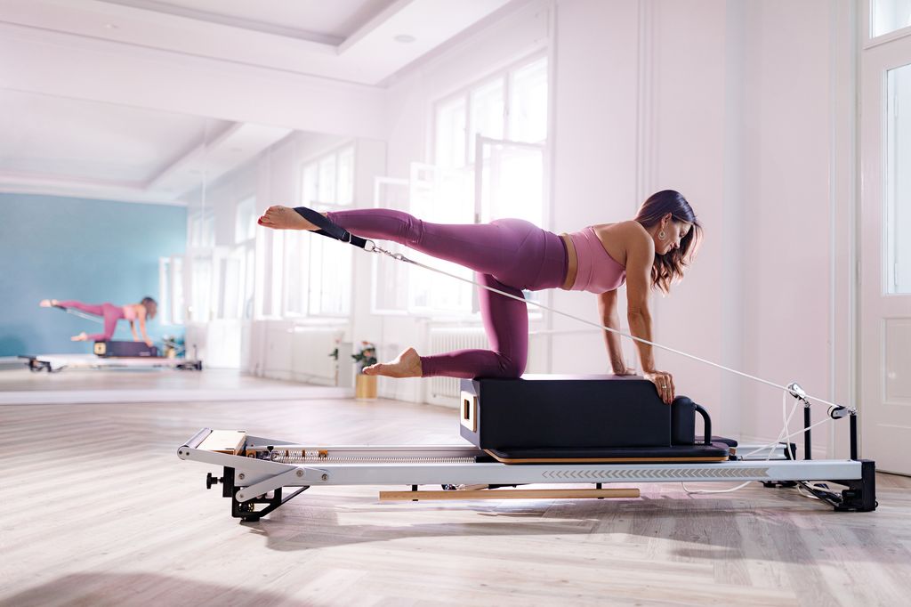 Happy female reformer doing stretching exercises on a Pilates machine in a health club