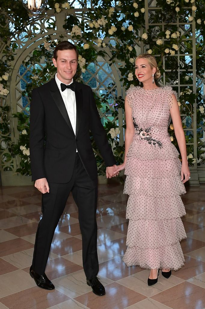 Ivanka stands in a light pink, tiered dress with black polka dots and floral detail, holding her husband’s hand. They’re dressed formally in a beautiful, flower-filled in the Booksellers Area of the White House to attend a state dinner honouring French President Emmanuel Macron.