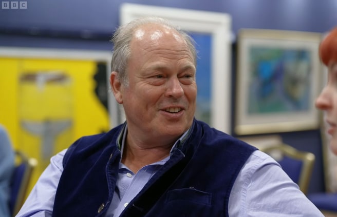 Man in blue shirt sitting in front of wall of paintings