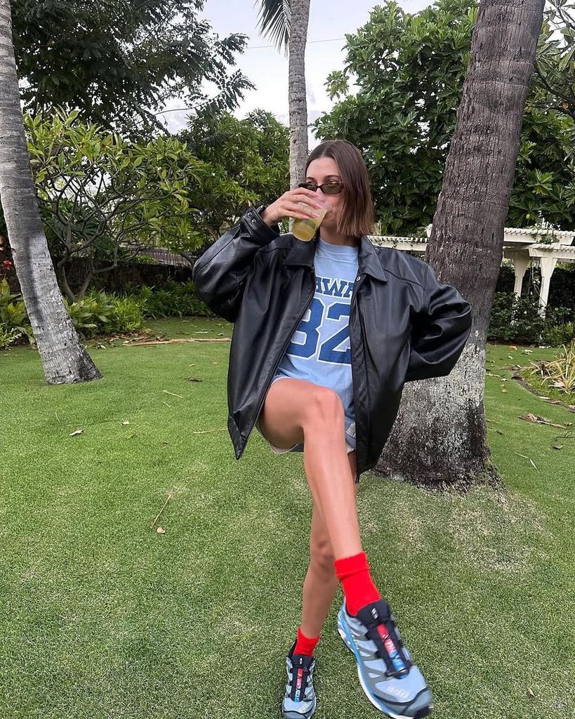 Hailey Bieber drinking from a cup while lifting her leg in her garden