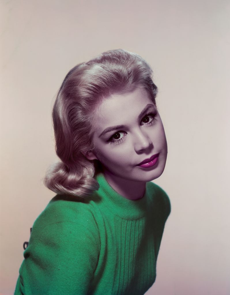 Sandra Dee est assise et regarde la caméra dans un pull vert avec un regard puissant vers la caméra.