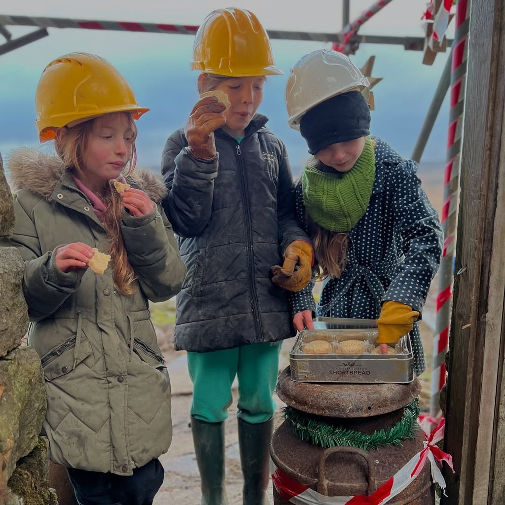 Three of Amanda's daughters eating snacks while wearing hard hats on construction site at their farm