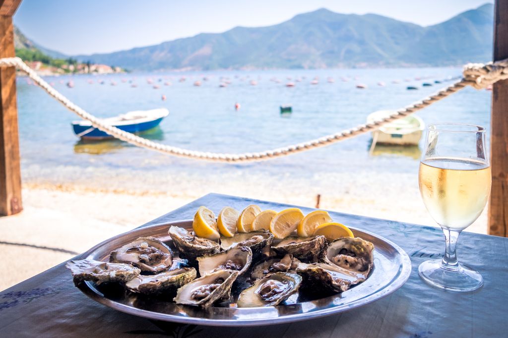 Mark McShane, expert en certificat d'hygiène alimentaire, révèle 7 aliments qui «peuvent entraîner une maladie grave» lors de voyage 5 Huîtres dans une assiette blanche avec du citron et un verre de vin sur une table en bois isolée sur blanc