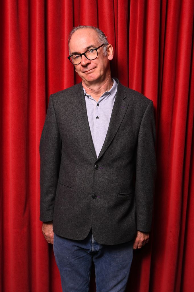 Paul Ritter in a grey suit in front of a red background