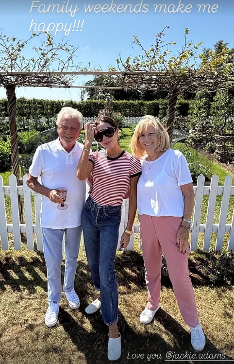 Victoria Beckham standing in between her parents outside with their vegetable garden in the background
