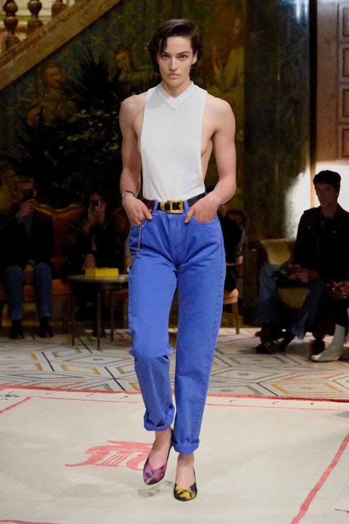 A model wears a skinny white vest and high waisted blue trousers with pumps