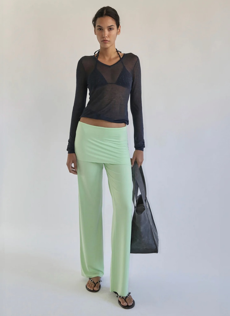 A model poses in green pants and a sheer top