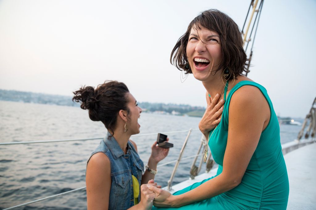 Two women getting engaged and laughing with joy on a sailboat.