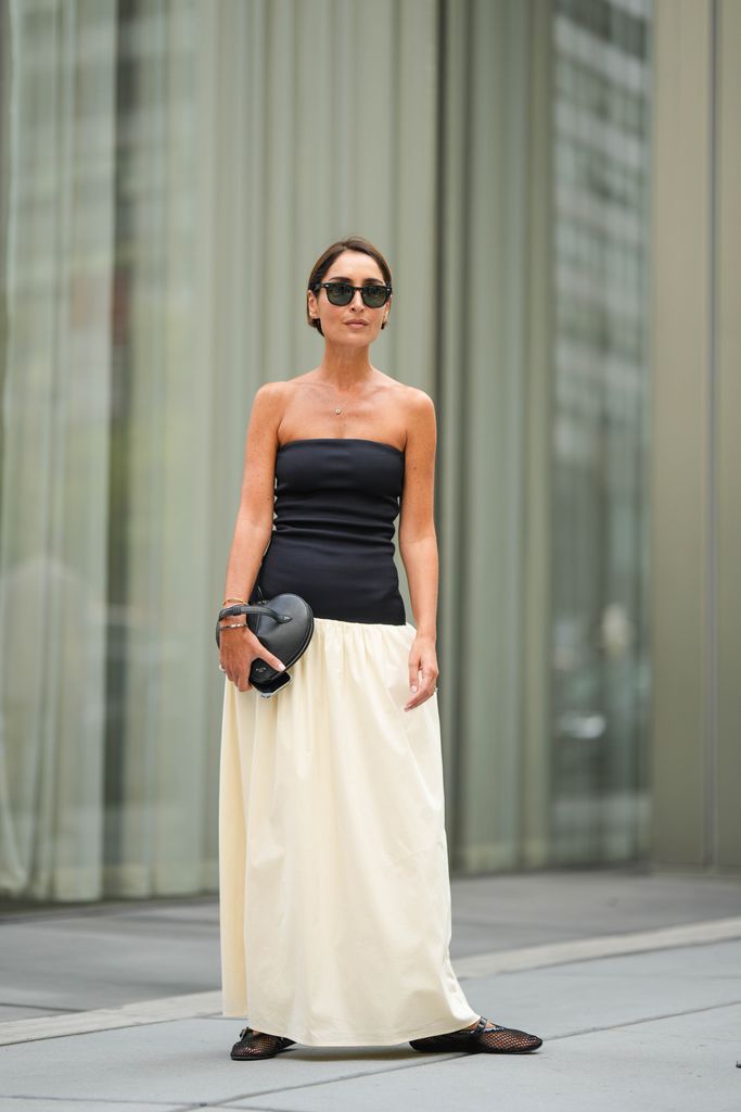 Geraldine Boublil wears a black off-shoulder top, a heart-shaped bag, a white maxi skirt, mesh shoes, outside Proenza Schouler, during New York Fashion Week