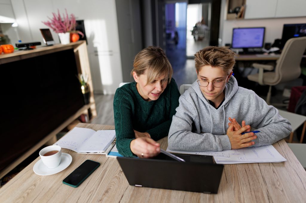 Mother and teenage boy doing some homework together. Mother is helping son with his lessons