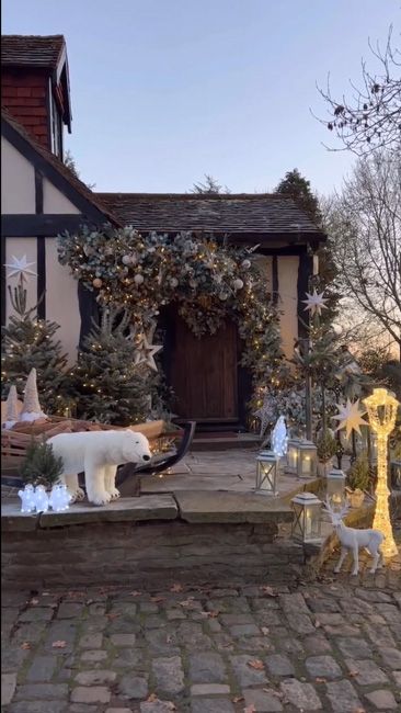 the outside of staceys home with an arch covered in baubles a stuffed polar bear and dozens of small christmas trees and lanterns surrounding a wooden sleigh