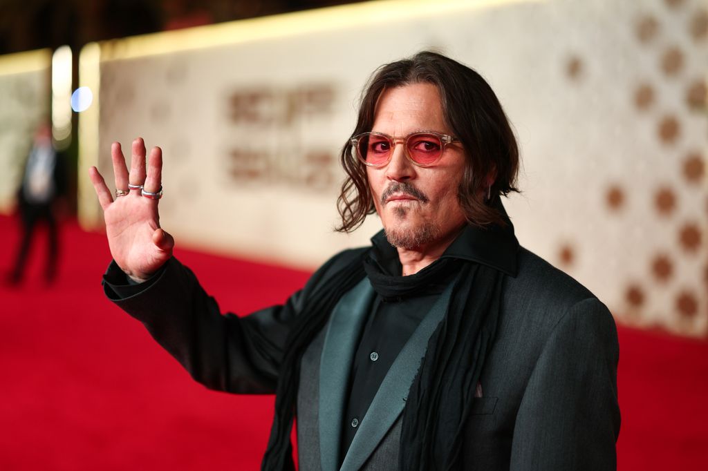 Johnny Depp se tient sur le tapis rouge et lève la main en signe de la main.