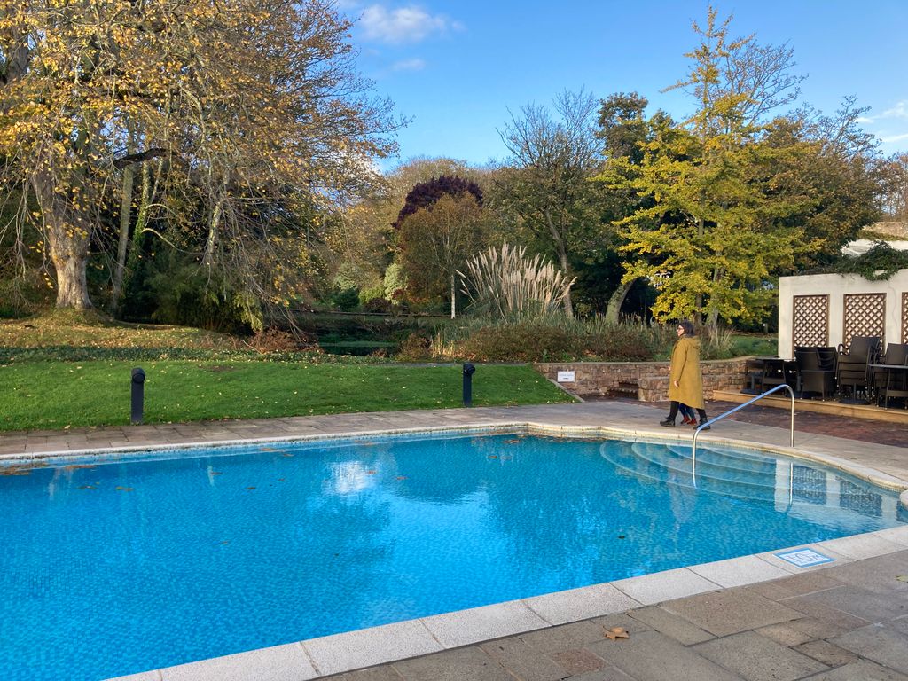 An outdoor swimming pool with women in yellow long coat walking round it