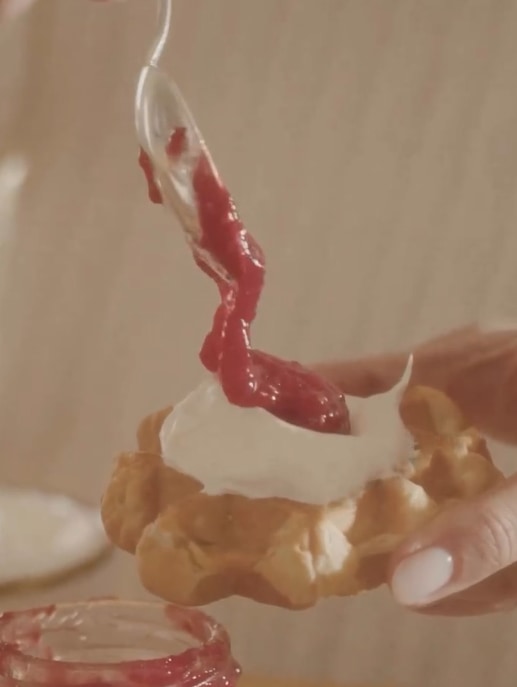 Meghan spooning jam and cream onto a waffle