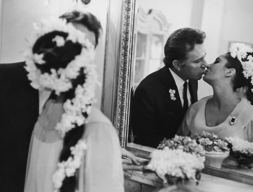 Richard Burton and Elizabeth Taylor kissing in wedding outfits in front of a mirror