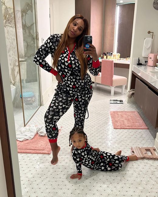 a photo of serena and her little girl in a large bathroom as they each strike a pose for the camera with serena standing with her hand on her hip and daughter seated on the floor and they both wear black pyjamas that are covered in white hearts with red stripes