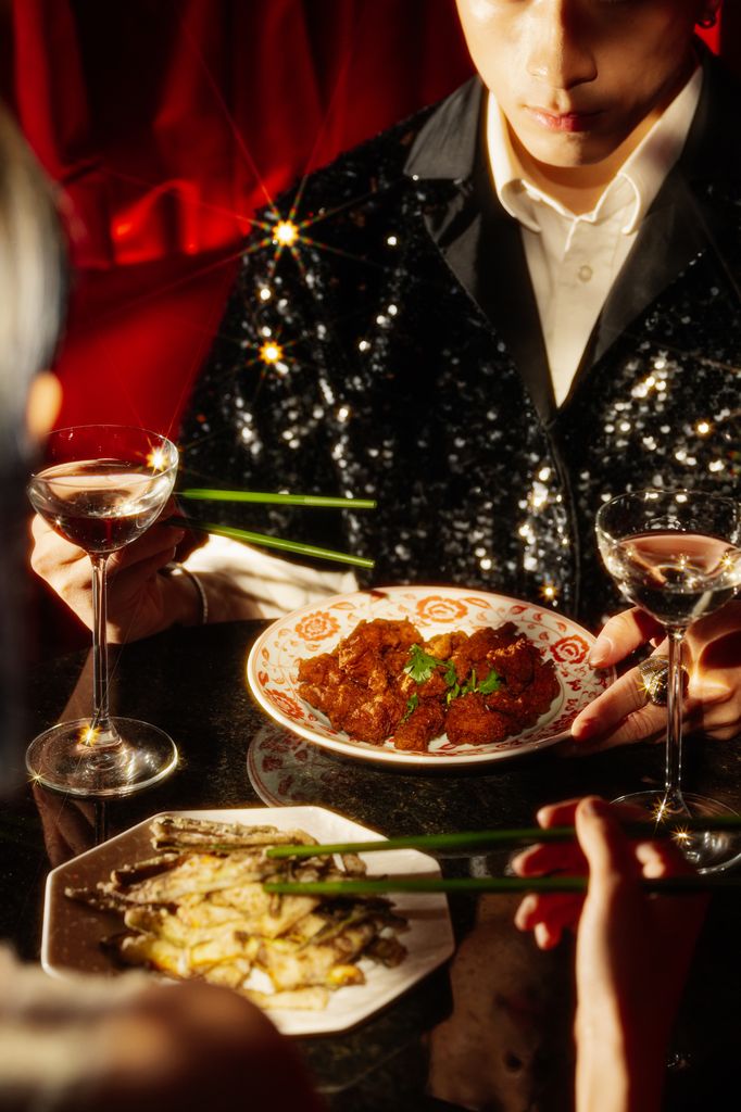 Man in glittery suit holding chopsticks next to a table of food and drink