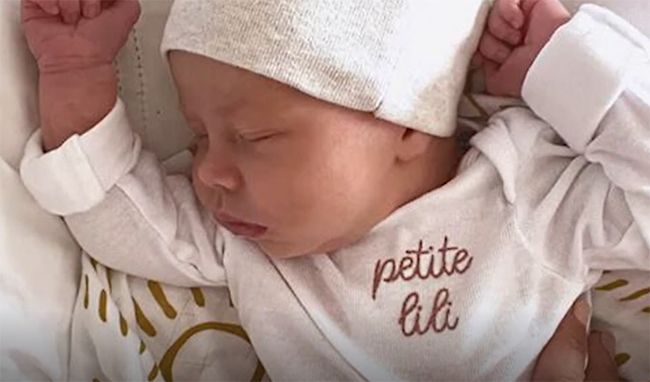 lilibet as a newborn with her hands in the air and a personalised babygrow
