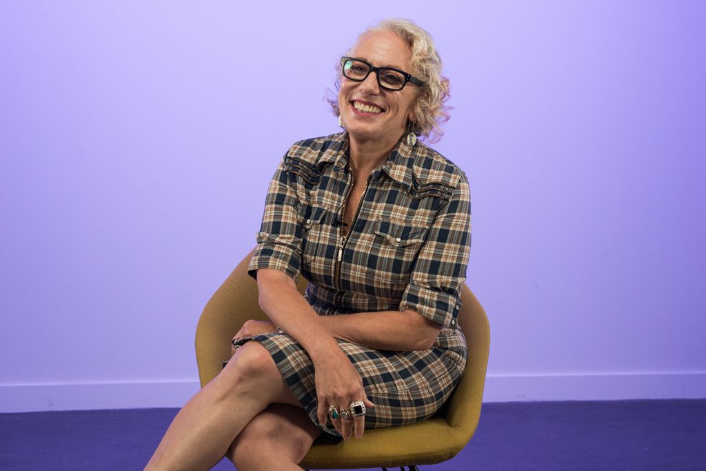 Woman in check dress smiling against a purple background 