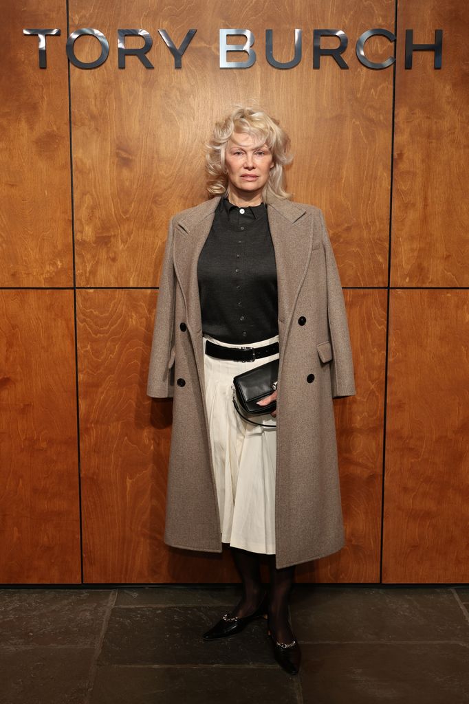 Pamela Anderson en pardessus beige et jupe blanche chez Tory Burch automne/hiver 2026 lors de la Fashion Week de New York 
