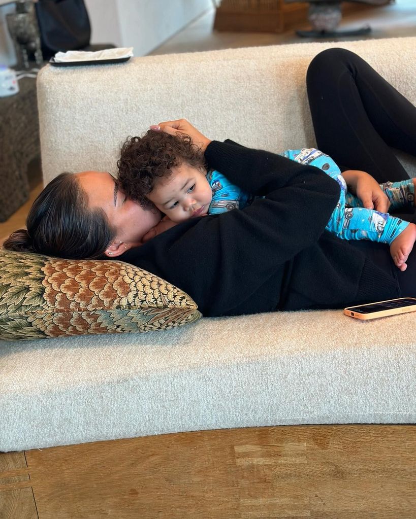 Chrissy Teigen lying on couch cuddling baby son Wren